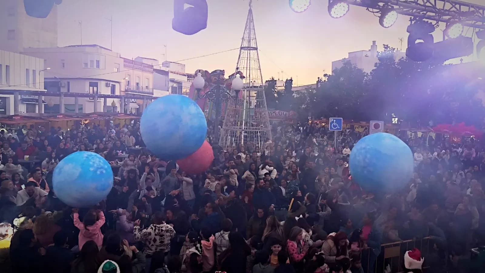 Bolas gigantes azules sobre el público de una plaza con árbol de luces